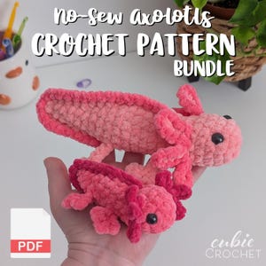 Puede incluir: Se muestran dos ajolotes de ganchillo rosas, uno grande y otro pequeño. El ajolote más grande se sostiene en una mano. La imagen incluye el texto "No-sew axolotls CROCHET PATTERN BUNDLE" y un icono PDF. Los ajolotes tienen ojos negros.