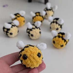 May include: A collection of handmade crochet bees. Each bee features a yellow body with black stripes, black eyes, and white wings. These plush toys are perfect for children or as decorative items.
