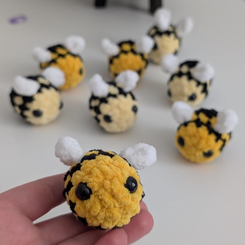 May include: A collection of handmade crochet bees. Each bee features a yellow body with black stripes, black eyes, and white wings. These plush toys are perfect for children or as decorative items.