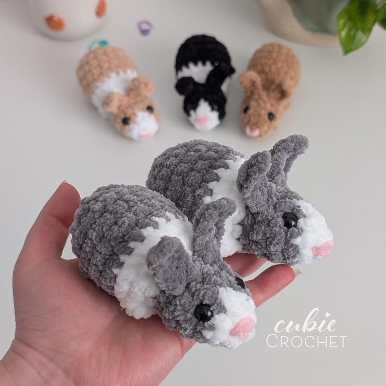 Op de afbeelding: Handgemaakte gehaakte cavia's en konijnen in verschillende kleuren, waaronder grijs, bruin en zwart. De pluche dieren hebben roze neuzen en zwarte ogen. De afbeelding bevat ook de tekst "cubie CROCHET".