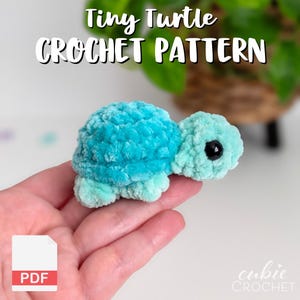 May include: A small, plush, crocheted turtle made of soft, fuzzy yarn in shades of teal and light blue. The turtle features a rounded shell, a small head with a black plastic eye, and four short legs. Text reads Tiny Turtle CROCHET PATTERN.