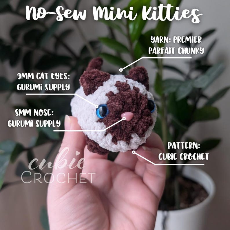 May include: A small crocheted cat toy in brown and white with blue eyes and a pink nose. The toy is made using the cubie crochet technique and is labeled "no-sew mini kitties". The yarn used is Premier Parfait Chunky.