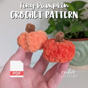 May include: Two small, plush, orange crochet pumpkins with brown stems. The image includes the text "Tiny Pumpkin Crochet Pattern" and a PDF icon. The Cubie Crochet logo is in the bottom right corner.