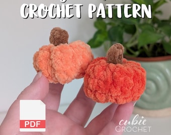 May include: Two small, plush, orange crochet pumpkins with brown stems. The image includes the text "Tiny Pumpkin Crochet Pattern" and a PDF icon. The Cubie Crochet logo is in the bottom right corner.