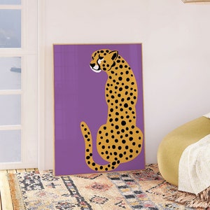 May include: A purple and yellow cheetah print art print hanging on a white wall above a yellow armchair with a white throw blanket. The armchair is on a rug with a geometric pattern.