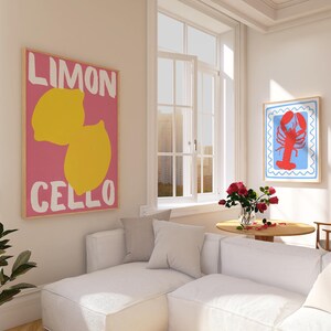 May include: Two framed art prints hang on a white wall. One features a pink background with yellow lemons and the words "LIMON CELLO." The other has a red lobster on a blue background with a white border. A white sectional sofa and round table are in the room.