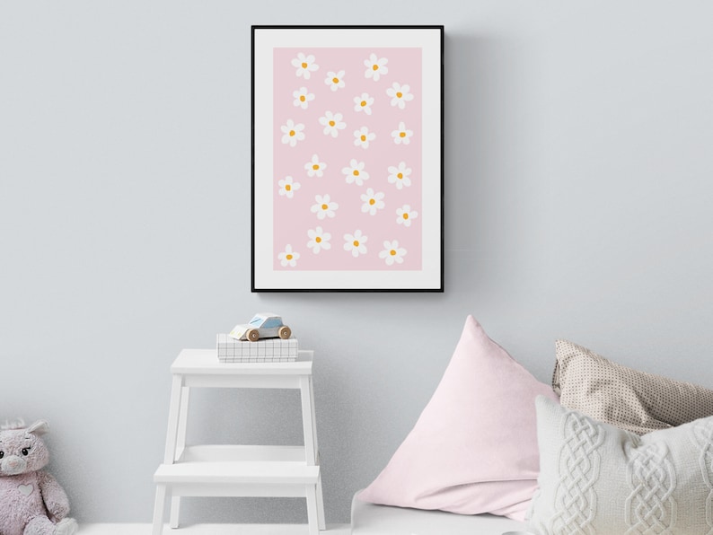 May include: A framed print with a pink background and white flowers with yellow centres. The print is hanging on a light grey wall.