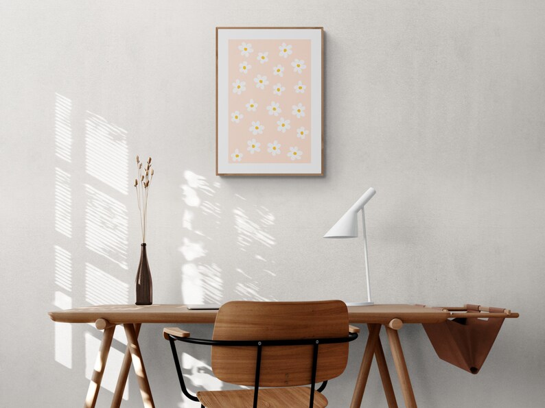 May include: A light wood desk with a white lamp, a chair, and a framed print of white flowers on a pink background.