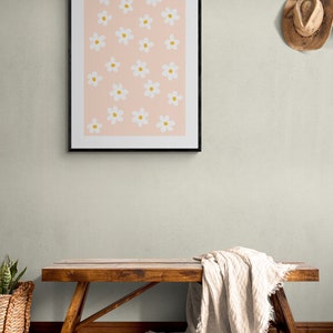 May include: A framed print with a pink background and white flowers with yellow centers. A wooden bench with a white blanket draped over it is in the foreground.