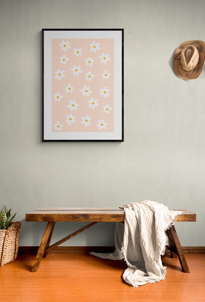 May include: A framed print with a pink background and white flowers with yellow centers. A wooden bench with a white blanket draped over it is in the foreground.