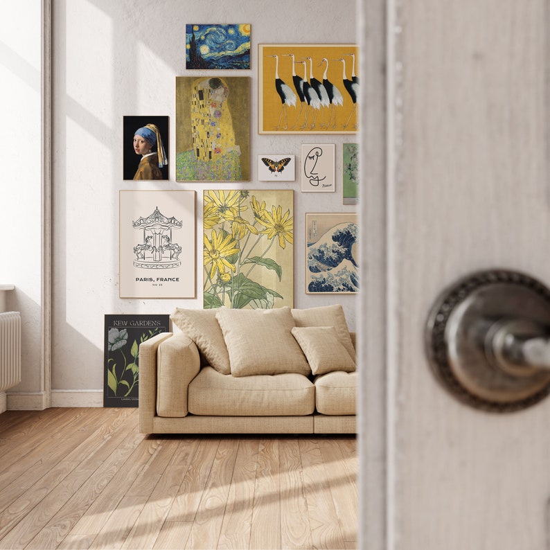 May include: A living room interior with a beige sofa and several framed prints on the wall. The prints include a floral design, a carousel, a starry night scene, a couple kissing, a group of birds, and a wave design. The wall is painted white and the floor is a light wood.