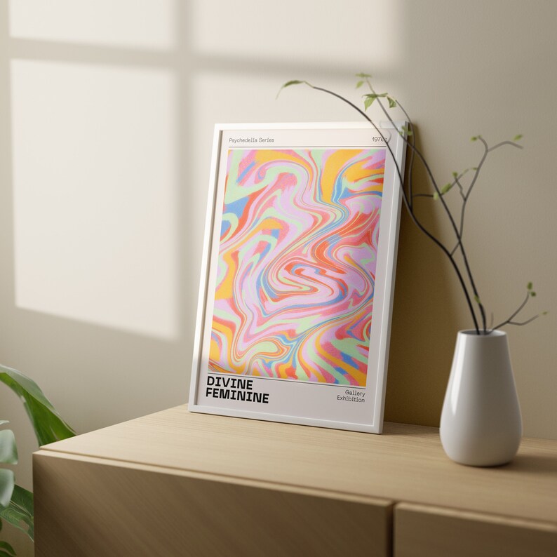May include: A framed print with a colorful abstract design in shades of pink, blue, yellow, and green. The text "DIVINE FEMININE" is at the bottom left corner of the print. The text "Gallery Exhibition" is at the bottom right corner of the print.