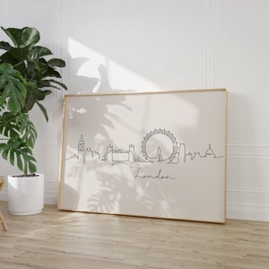 May include: A black and white line drawing of the London skyline, including the London Eye, Big Ben, and Tower Bridge. The drawing is on a white background and framed in a gold frame. The word "London" is written in cursive below the skyline.
