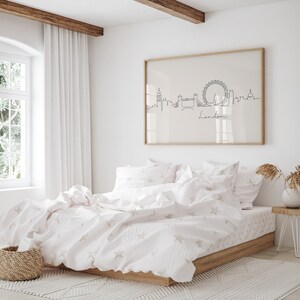 May include: A white bed with a white and pink star patterned duvet cover and matching pillowcases. A framed print of a line drawing of the London skyline with the word "London" underneath is hanging on the wall behind the bed.