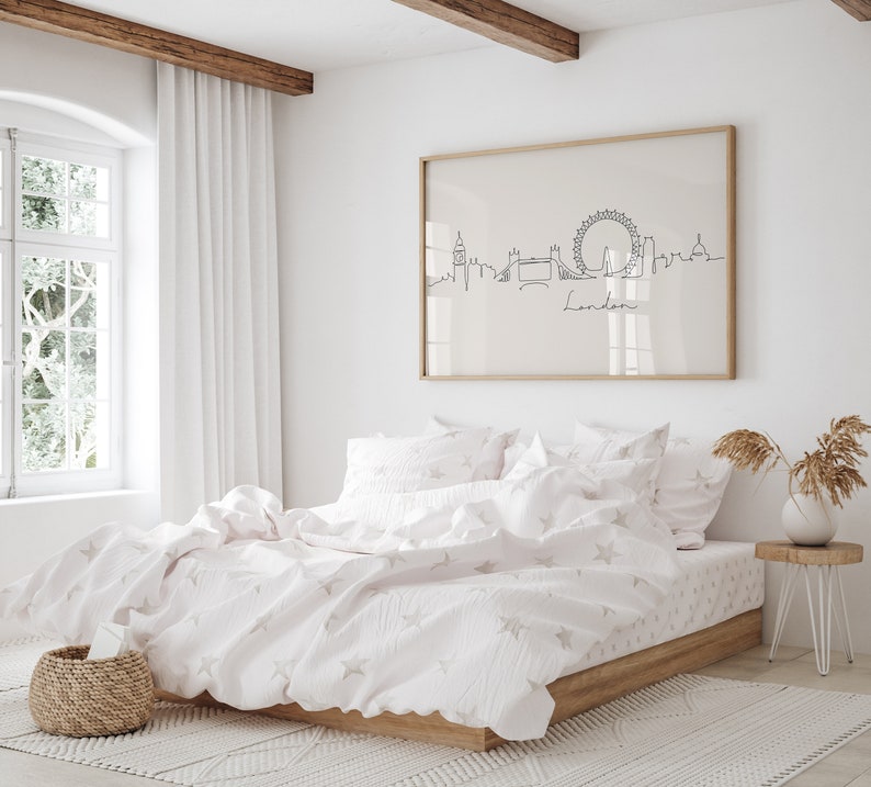 May include: A white bed with a white and pink star patterned duvet cover and matching pillowcases. A framed print of a line drawing of the London skyline with the word "London" underneath is hanging on the wall behind the bed.