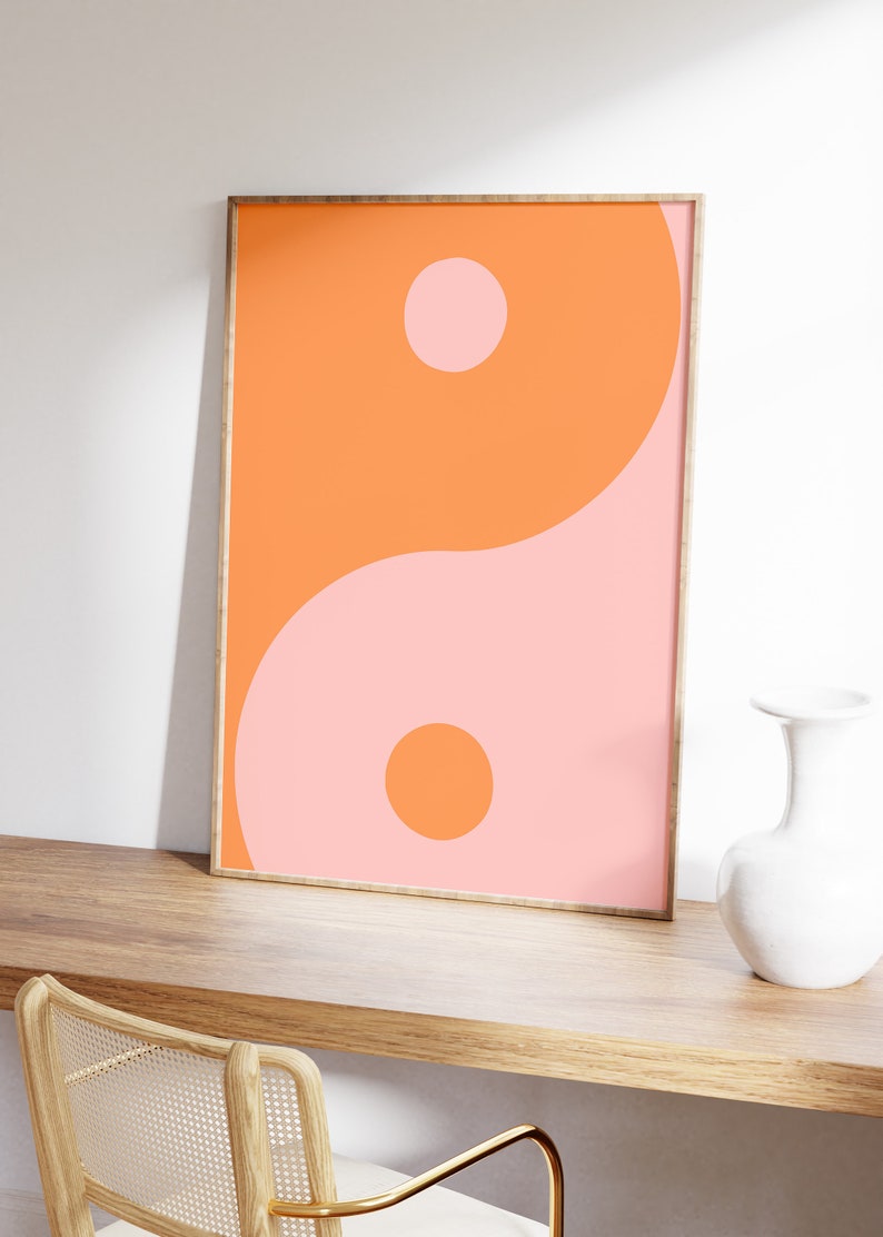 May include: A framed print of a yin yang symbol in orange and pink. The symbol is a circle with two halves, one orange and one pink, each containing a smaller circle of the opposite colour.