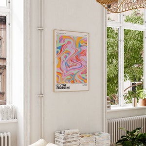 May include: A framed poster with a colorful abstract design in shades of pink, blue, yellow, and green. The text "DIVINE FEMININE" is printed in black at the bottom of the poster.