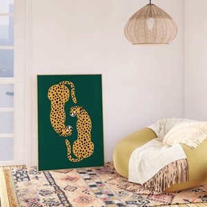 May include: A framed print of two stylized cheetahs in a green background. The cheetahs are facing each other and are in a curled position. The print is hanging on a white wall above a yellow armchair with a white throw blanket.