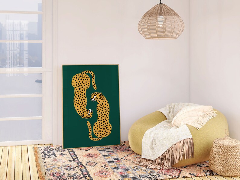 May include: A framed print of two stylized cheetahs in a green background. The cheetahs are facing each other and are in a curled position. The print is hanging on a white wall above a yellow armchair with a white throw blanket.