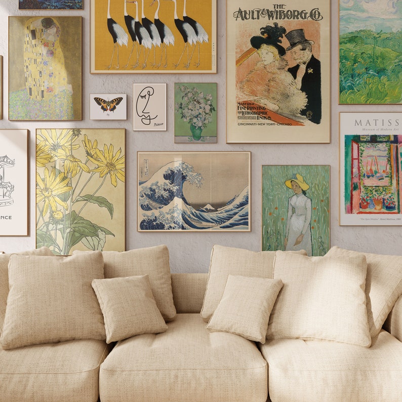 May include: A living room with a beige couch and pillows, decorated with various framed artwork. The artwork includes a painting of a wave, a painting of flowers, a painting of a couple, a painting of cranes, a painting of a woman in a hat, and a painting of a window with a view.
