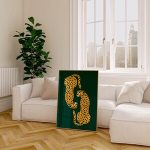 May include: A framed print of two stylized cheetahs in orange and black on a dark green background. The print is hanging on a white wall in a living room setting.