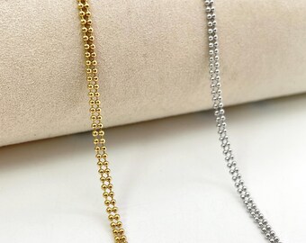 Peut inclure: Gros plan sur deux colliers délicats. L'un est de couleur or, l'autre de couleur argent. Les deux colliers présentent un double rang de petites perles rondes. Le collier doré est à gauche et le collier argenté à droite.