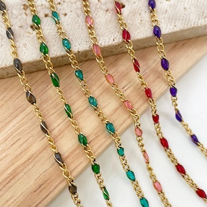 May include: Six gold-toned metal chains arranged vertically, each featuring small, oval-shaped enamel accents in distinct colors including black, green, teal, pink, red, and purple, integrated directly into the links of the chain design.