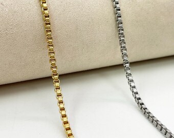 Peut inclure: Gros plan de deux colliers chaîne de type 'box chain', l'un doré et l'autre argenté. Les chaînes sont présentées sur un fond neutre, mettant en valeur leur design complexe à maillons carrés. Les chaînes sont délicates et élégantes.