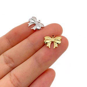 May include: Two metal bow charms, one gold and one silver. The charms are in the shape of a bow with a loop at the top for attaching to a necklace or bracelet.