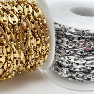Può includere: Primo piano di due bobine di catena. Una è dorata, l'altra argentata. Le maglie della catena sono ovali con una barra centrale. Le catene sono avvolte attorno a bobine bianche.