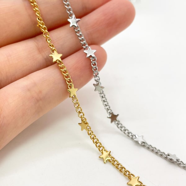Puede incluir: Dos cadenas metálicas delicadas, una en tono dorado pulido y otra en tono plateado brillante, cada una con pequeños dijes en forma de estrella espaciados uniformemente a lo largo de los eslabones, creando un componente de joyería decorativo.