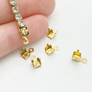 Puede incluir: Cinco cierres de metal dorado para la elaboración de joyas. Los cierres tienen una forma cuadrada con un pequeño bucle en un lado.