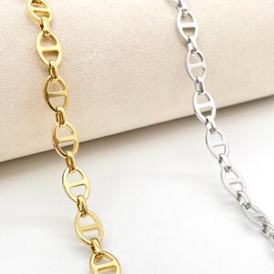 Puede incluir: Primer plano de dos collares con un diseño de eslabones de cadena. Un collar es de color dorado y el otro es de color plateado. Los collares se muestran sobre una superficie de color neutro.