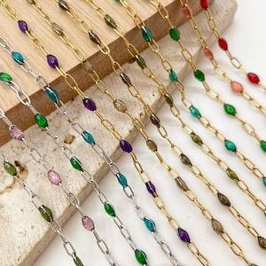 May include: A collection of metal chains featuring oval links interspersed with small, colorful, faceted beads. The chains are available in silver and gold tones, with beads in shades of green, purple, pink, red, and brown.