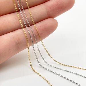 Puede incluir: Tres cadenas de eslabones delicados, dos en tono dorado y una en tono plateado, con eslabones rectangulares alargados. Las cadenas son finas y ligeras, mostrando un diseño sencillo con un acabado pulido que refleja la luz sobre el metal.