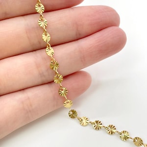 May include: A gold chain necklace featuring a series of small, circular, sunburst-patterned metal discs linked together. Each disc has a reflective, textured surface with radiating lines that catch the light, creating a bright, metallic appearance.