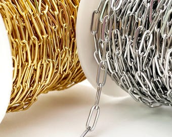 Könnte beinhalten: Nahaufnahme von zwei Kettenspulen. Eine Spule ist goldfarben und die andere silberfarben. Die Ketten haben ein längliches ovales Glieddesign. Die Ketten befinden sich auf weißen Spulen.