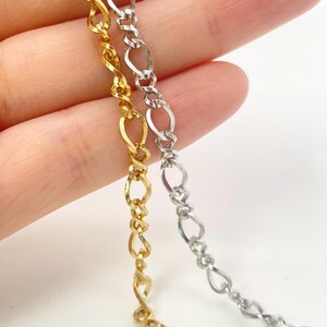 May include: Two metallic chains, one in a bright gold tone and one in a silver tone, featuring a repeating twisted oval link design. Each chain consists of interconnected elongated loops that create a continuous, textured, and flexible metal strand.