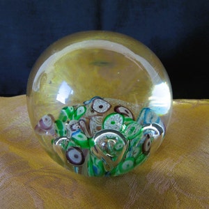 May include: A clear glass paperweight with a swirling pattern of green, white, and purple glass inside.