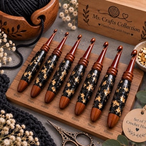 May include: A set of seven crochet hooks with wooden tips and black handles featuring gold leaf accents, arranged on a wooden display board labeled with sizes from 4mm to 10mm. The board includes the text Set of 7 Crochet Hooks and Ms. Crafts Collection.