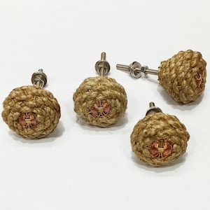 Może przedstawiać: Cztery brązowe gałki do szafek z juty z miedziano-złotym akcentem w środku. Gałki mają srebrną śrubę z tyłu.