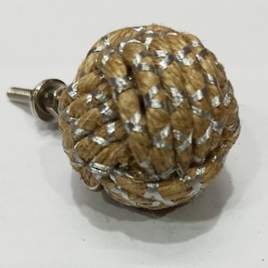 Peut inclure: Un bouton de porte en corde marron et argent avec une vis en métal. La corde est tissée en forme de nœud et présente des accents argentés.