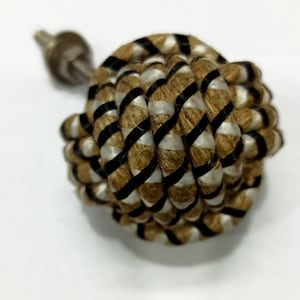 Op de afbeelding: Een ronde, bruin en zwarte touwknop met een metalen schroef. Het touw is diagonaal geweven.