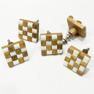 May include: Four square wooden cabinet knobs with a checkered pattern of brown and white. The knobs have a silver metal screw on the back.