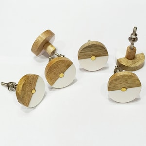 May include: Five round wooden cabinet knobs with a white half circle and a gold dot. The knobs have a silver screw.