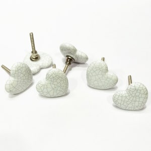 May include: Five white ceramic heart-shaped drawer pulls with a crackled glaze finish and silver metal screws.