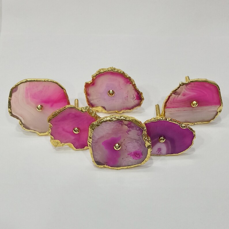 Op de afbeelding: Zes roze en witte agaat-ladegrepen met gouden rand. Elke greep heeft een gouden knop in het midden.