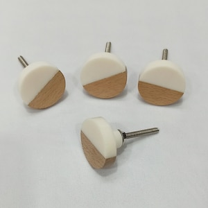 Puede incluir: Cuatro pomos redondos para armario en blanco y madera con tornillos plateados.