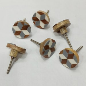 May include: Six round wooden cabinet knobs with a geometric pattern of white, gray, and brown. The knobs have a silver screw.