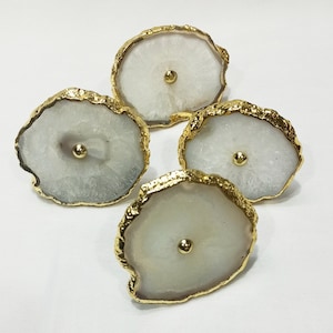 Puede incluir: Cuatro tiradores de cajón de ágata blanca con ribete de metal dorado. Cada tirador tiene un pomo redondo de oro en el centro.